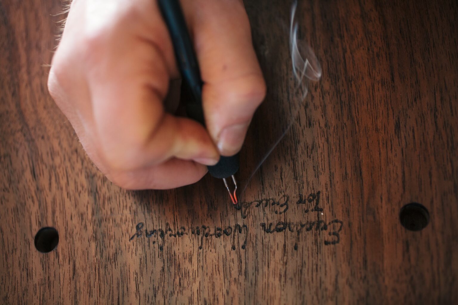 A hand signs the wood of an Erickson Wood Working piece.