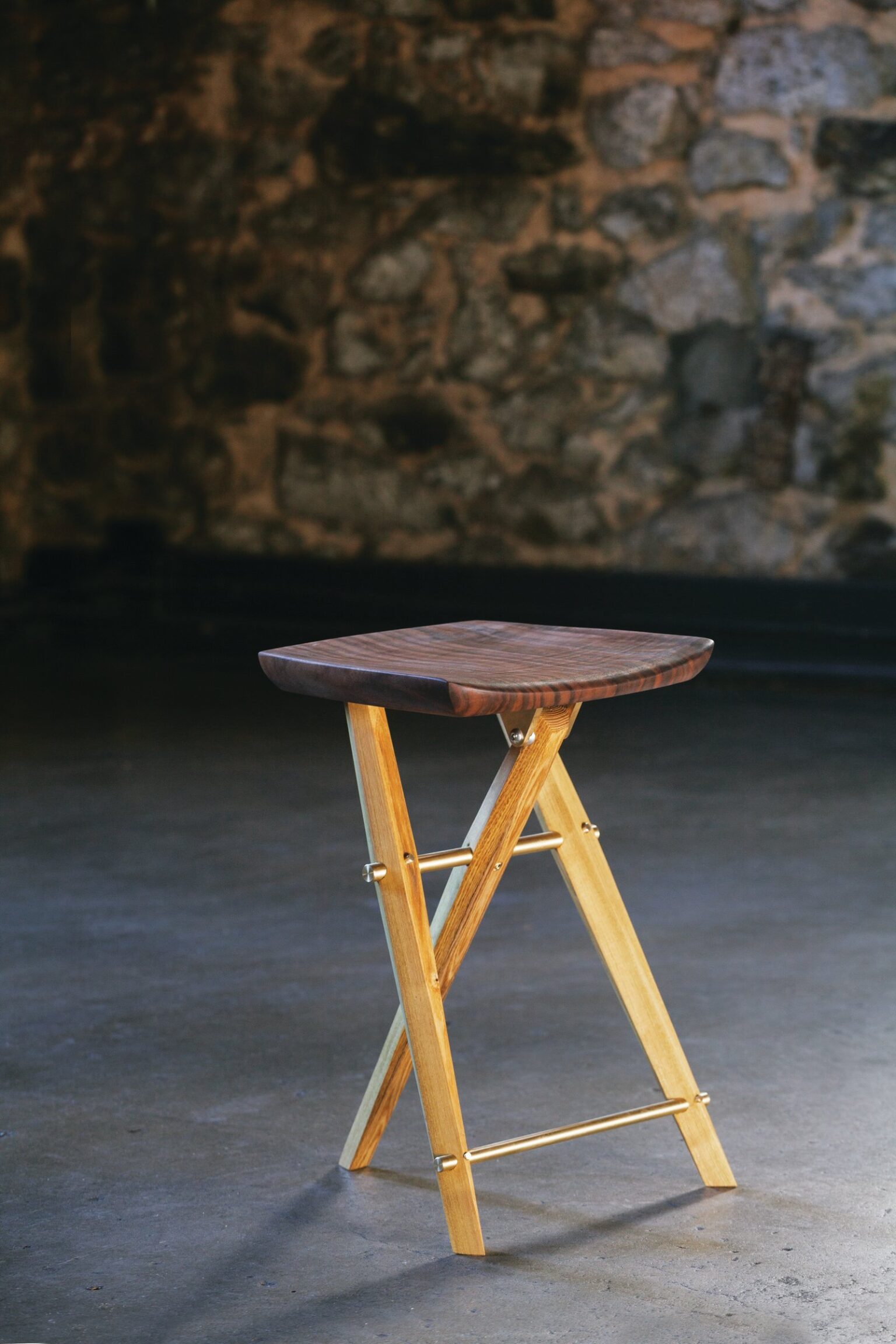 A wooden stool in front of a stone wall.