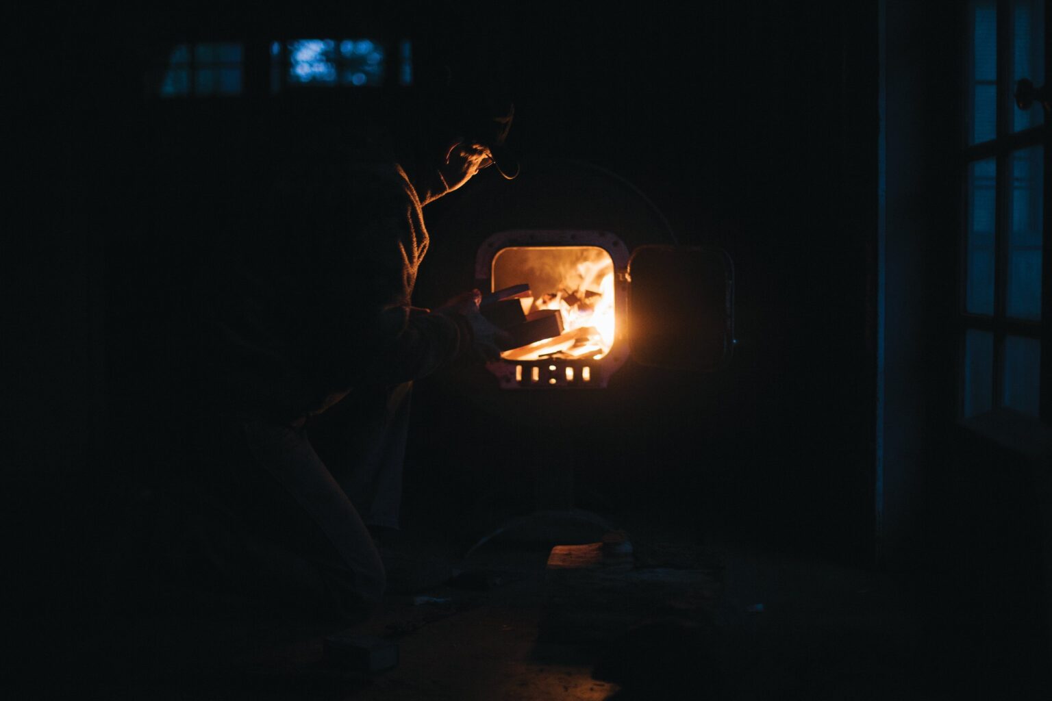A person tends a wood-burning stove in a dark interior.